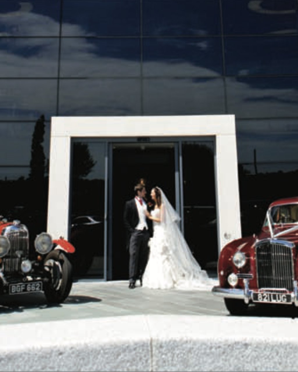 A bride and groom at the main entrance of Brooklands Hotel, Weybridge, Surrey, with vintage wedding cars
